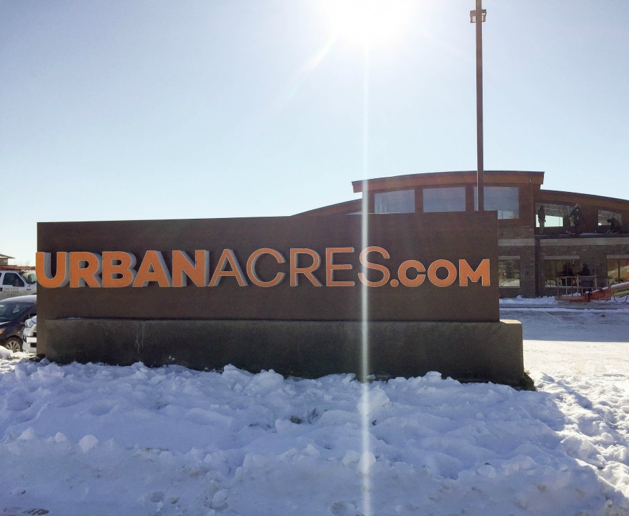 A monument sign reading urbanacres.com in the snow on a sunny day