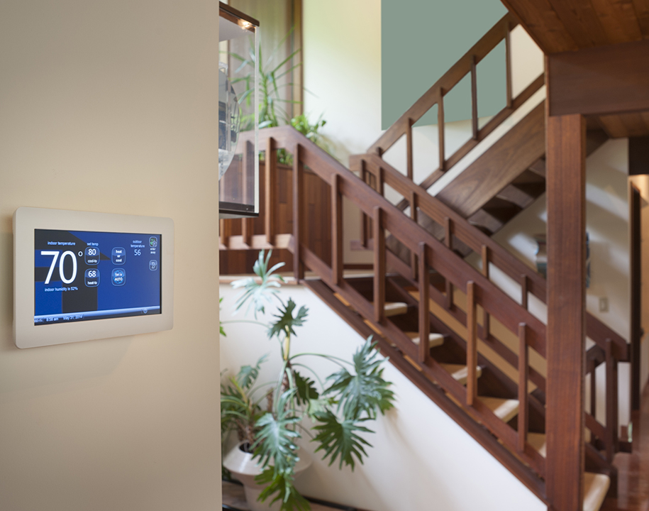 Smart thermostat on a wall next to a wooden staircase