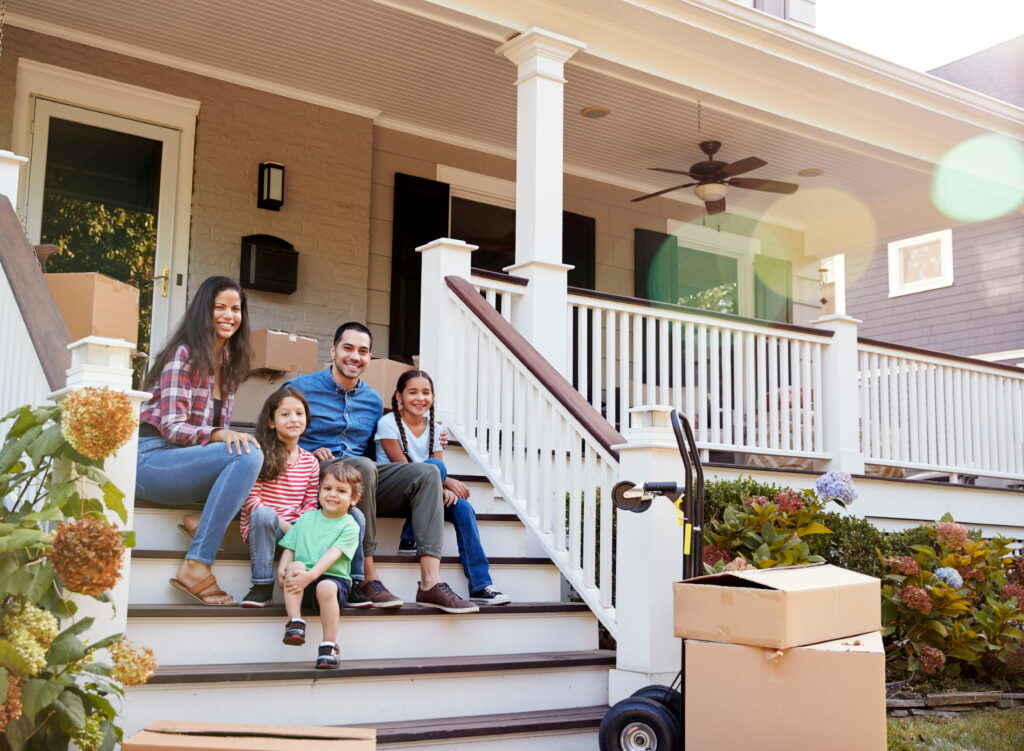 Family sitting on the steps of their new home on moving day