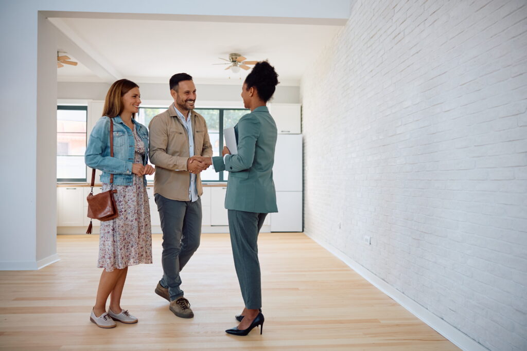 Happy couple of real estate buyers handshaking with their agent in new house