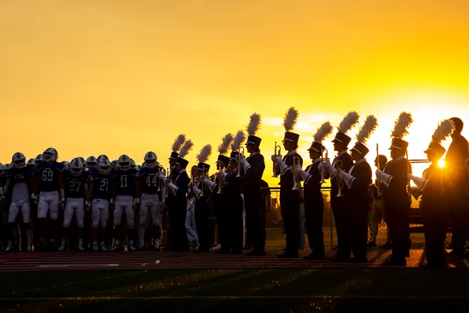 Clear Creek Amana High School football team and marching band on field at sunset