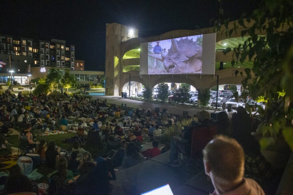 Audience members watching a dinosaur on screen at FilmScene in the Park in Iowa City