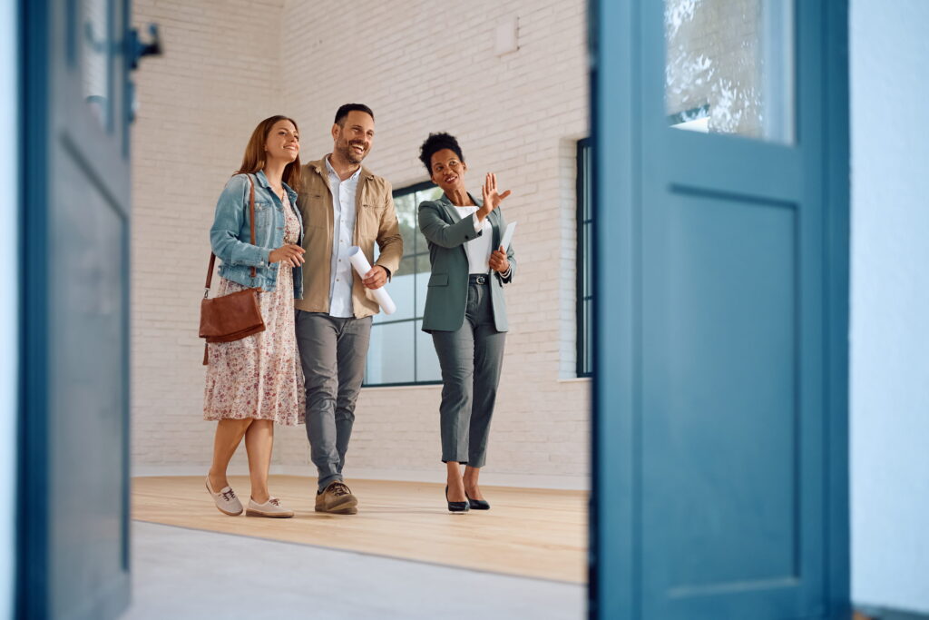 Happy African American real estate agent showing house for sale to couple interested in buying it
