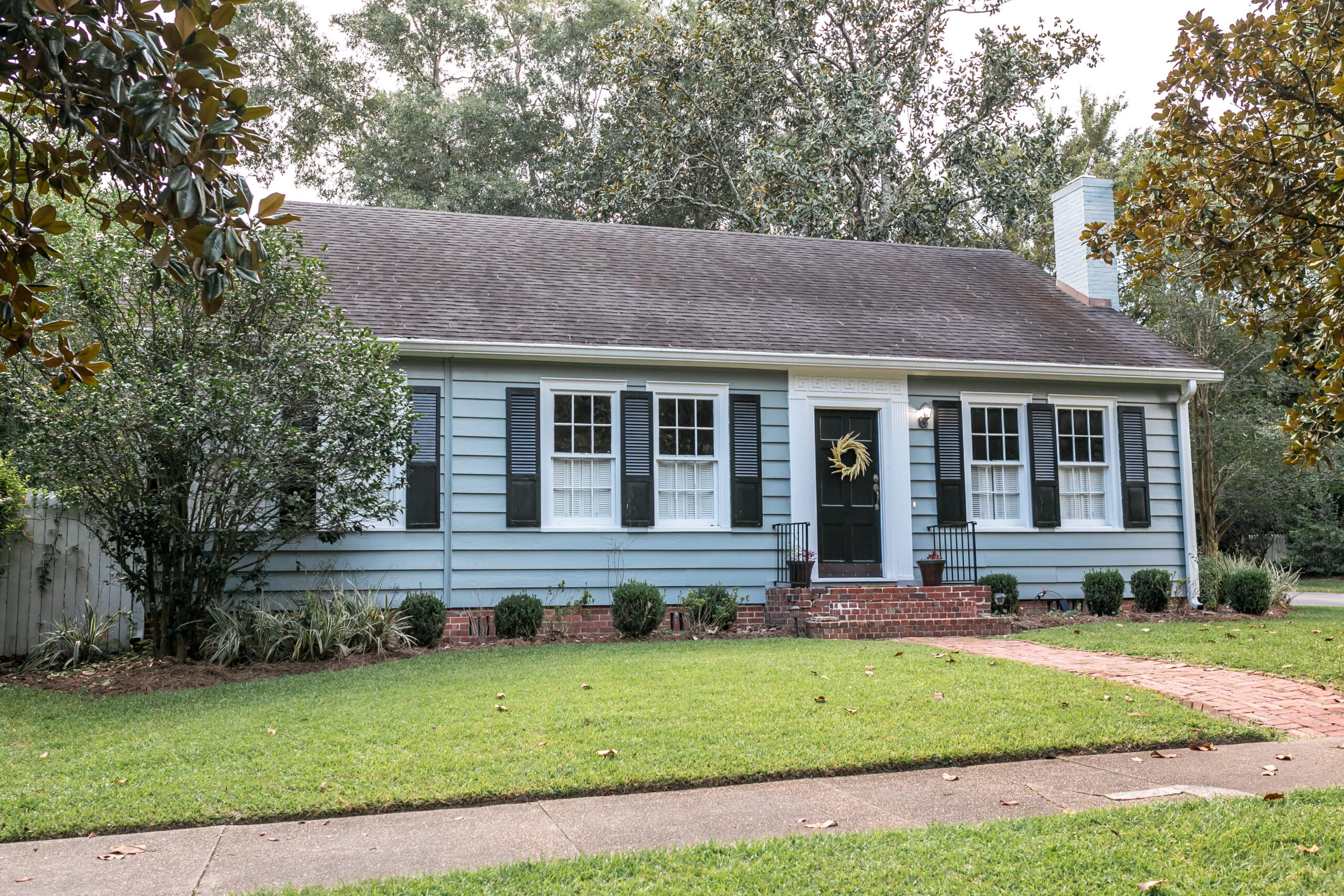 Small older blue cottage with a green front lawn and sidewalk, featured in a guide to selling a house as-is